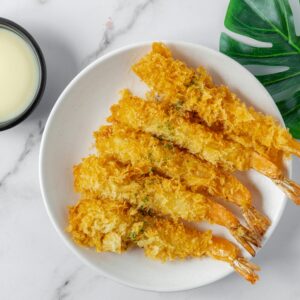A plate of crispy shrimp with white dipping sauce on a marble background.