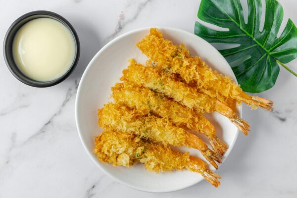 A plate of crispy shrimp with white dipping sauce on a marble background.