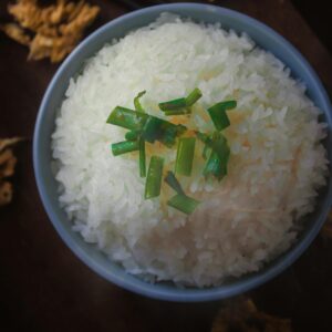 A close-up of a bowl of steamed white rice garnished with chopped green onions, showcasing elegant food presentation.